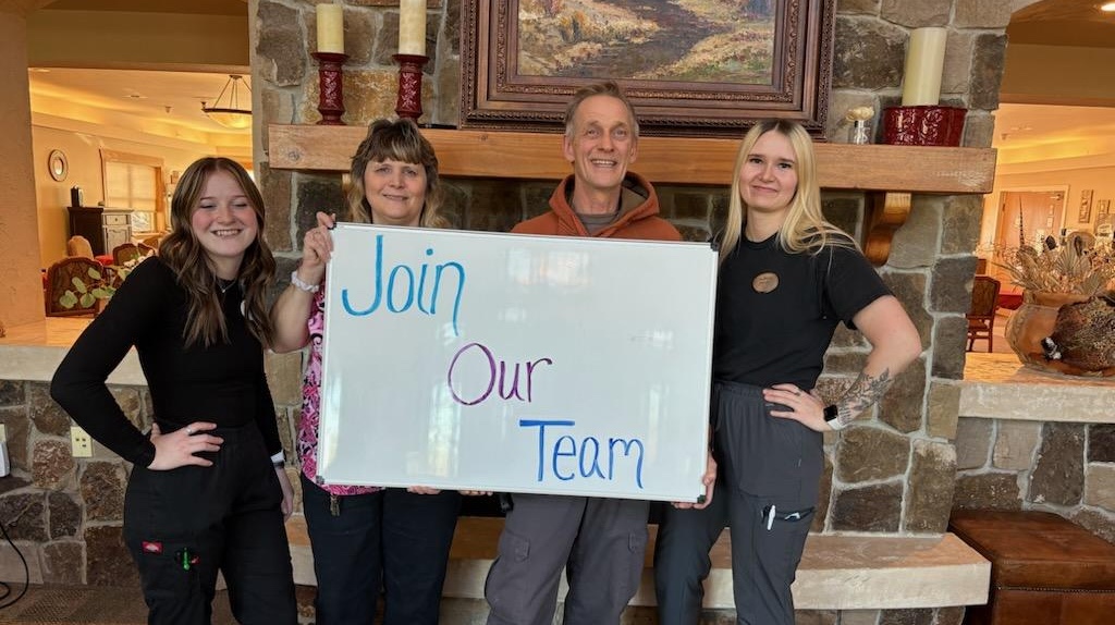 Community staff members holding a welcome sign encouraging new applicants to join the team.